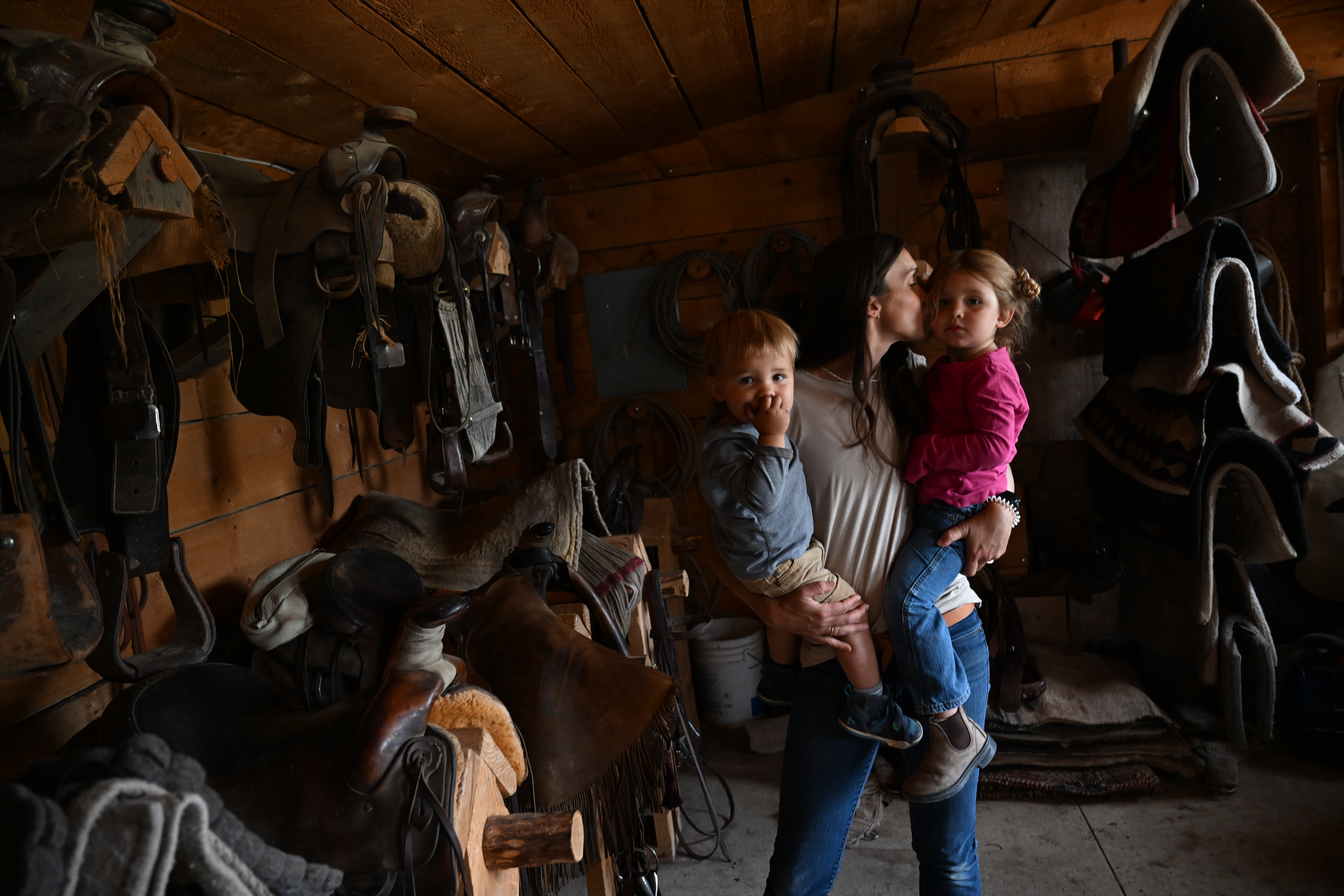 Madi Phillips gives her daughter Dean, 4, a kiss as she holds both Dean and Duke V, 3, left, in her arms while working in the leather shop at Chico Basin Ranch on June 29, 2023. Madi oversees making all of the leather products that Ranchlands sells as well as gear for apprentices and ranchers. (Photo by Helen H. Richardson/The Denver Post)