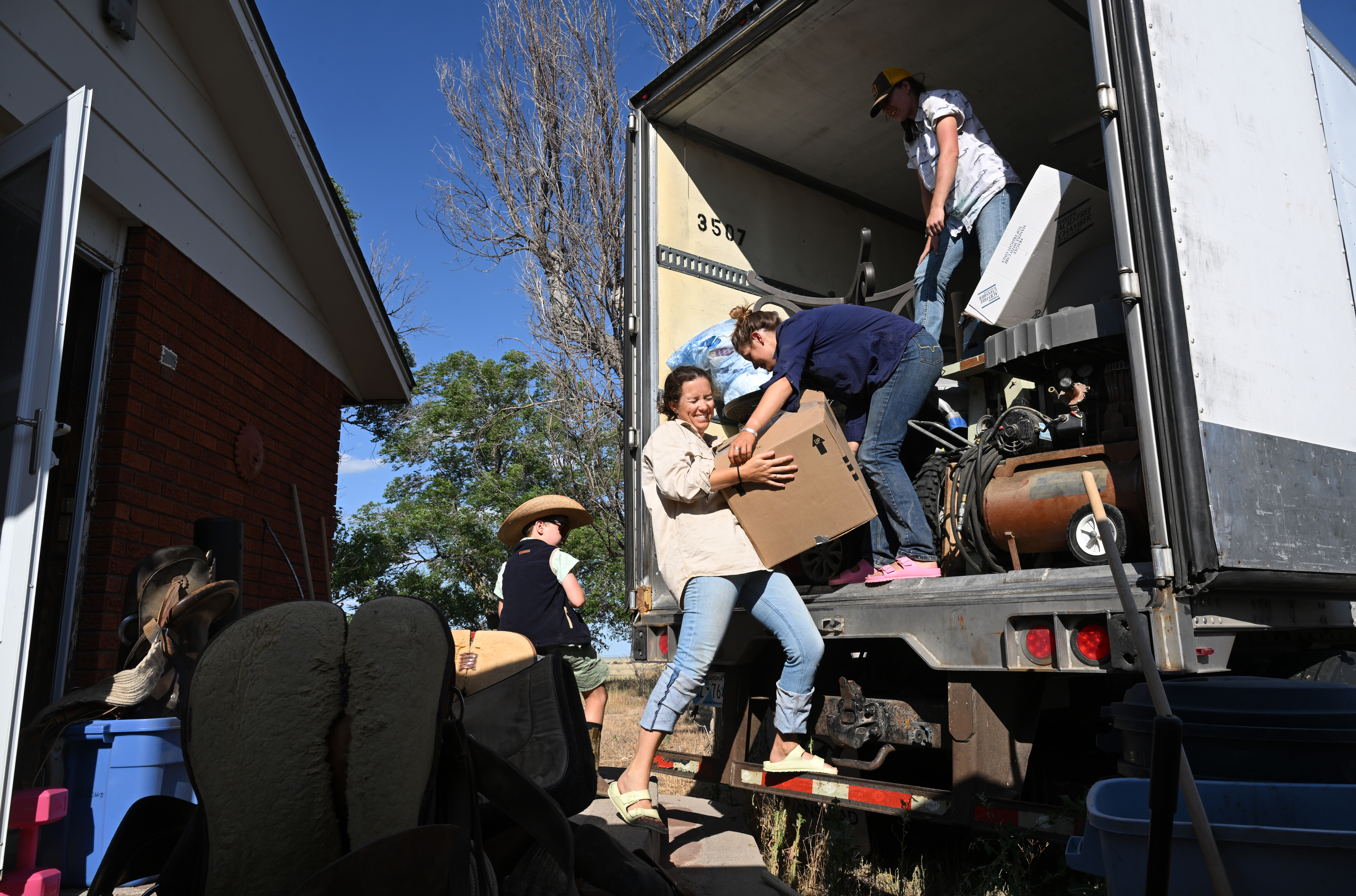 Tess Leach, center, gets help from her sister Grace and friend Tillie Mackenzie, right, loading up heavy boxes onto a large semi-truck while in the process of moving out of the house she has lived in for almost twenty years at Chico Basin Ranch on June 29, 2024. (Photo by Helen H. Richardson/The Denver Post)