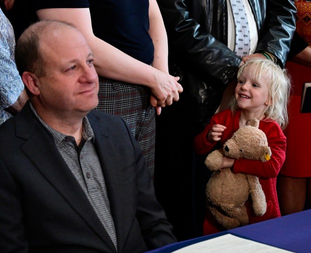 Mollie Jenks, 3, Colorado Sen. Tom Sullivan's granddaughter, holding her stuffed animal "Teddy," tries to get Colorado Gov. Jared Polis' attention before Polis signed Senate Bill 3 into law in the governor's office at the State Capitol in Denver on Thursday, April 10, 2025. SB25-003 is a gun-control bill that institutes a permitting and background check system before someone can purchase certain semi-automatic weapons. Sullivan's son Alex Sullivan, was killed in the Aurora theater shooting in 2012. (Photo by Andy Cross/The Denver Post)